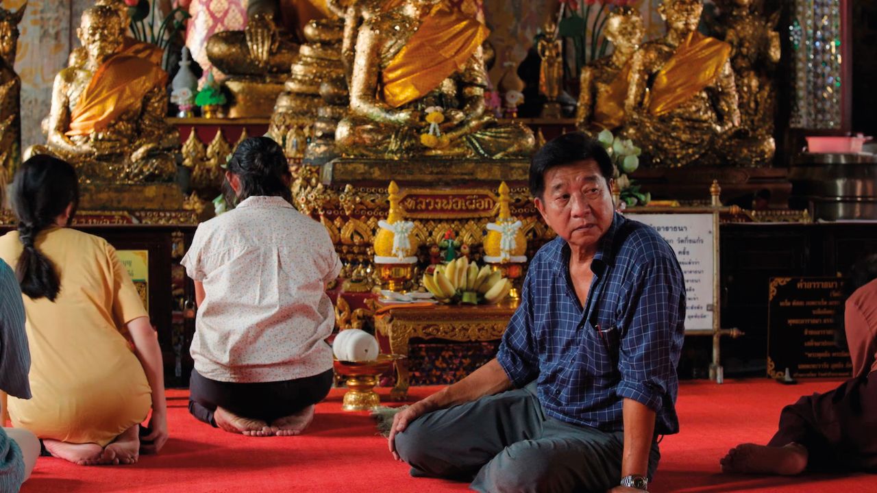 Un hombre sentado frente a un altar budista con familiares en una escena de 9 Temples to Heaven