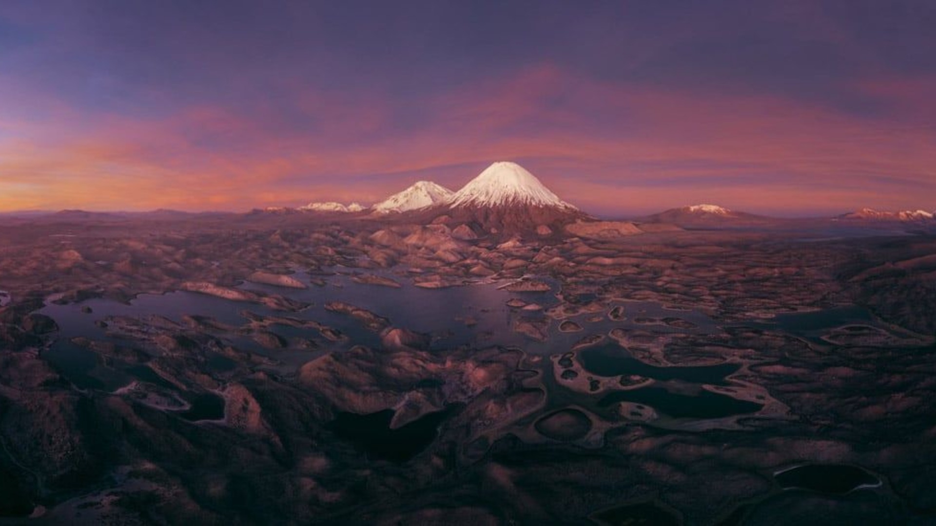 Panorama aéreo del volcán Parinacota y el Pomerape con lagos de altura bajo luz magenta