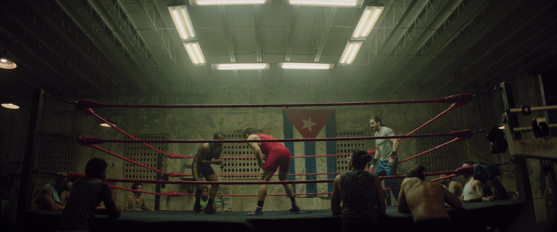 Combate de lucha en un gimnasio con la bandera de Puerto Rico, en una escena de Espinal